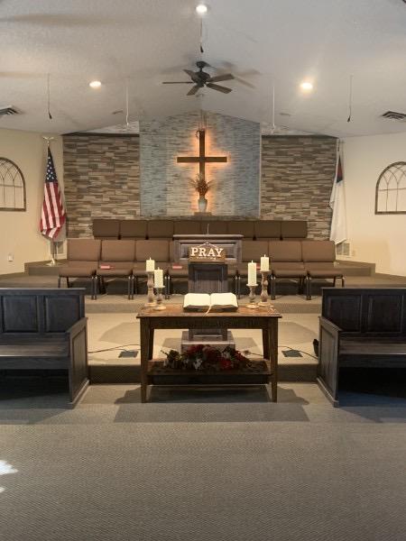 Open Bible at the pulpit beneath the illuminated cross inside Faith Baptist Church.